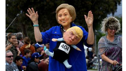 Una mujer lleva una máscara de Hillary Clinton, y carga un muñeco de Donald Trump durante un desfile de Halloween en Long Beach, California,