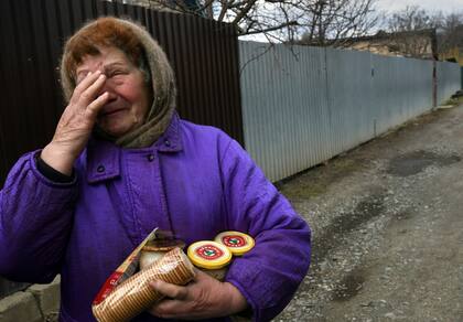 Una mujer llora mientras recibe ayuda alimentaria en medio de escombros de guerra y cuerpos tirados en las calles de Bucha