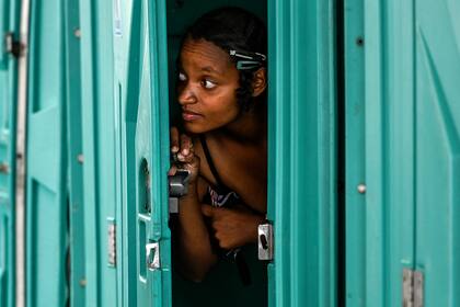 Una mujer mira por la puerta de la cabina de un baño químico antes de bañarse en un área provista para personas sin hogar en medio de la pandemia de coronavirus en Medellín, Colombia, el 23 de junio de 2020