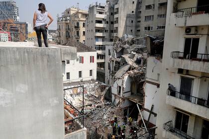 Una mujer observa desde una azotea mientras los rescatistas excavan entre los escombros de un edificio gravemente dañado en Beirut, la capital del Líbano, en busca de posibles sobrevivientes de una mega explosión en el puerto adyacente hace un mes, después de que los escáneres detectaran un pulso, e