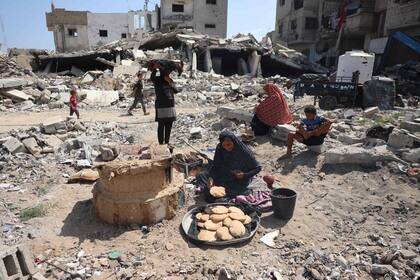 Una mujer palestina hornea pan en un horno improvisado mientras está sentada sobre los escombros de los edificios destruidos por el bombardeo israelí, mientras algunos residentes regresan a la ciudad de Khan Younis, en el sur de la Franja de Gaza, el 30 de junio de 2024, en medio del conflicto en curso entre Israel y el grupo militante palestino Hamas.