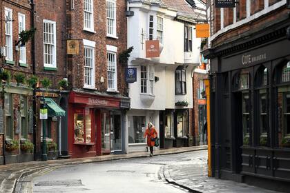 Una mujer pasa frente a las tiendas, cerradas temporalmente debido a las restricciones actuales del coronavirus, en York, noroeste de Inglaterra, el 6 de enero de 2021