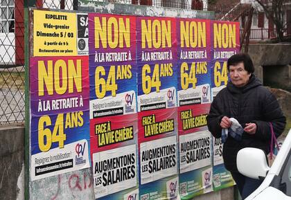 Una mujer pasa junto a carteles que dicen "No a la jubilación a los 64" en Saint Pee sur Nivelle, en el suroeste de Francia, el lunes 6 de marzo de 2023.