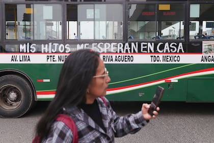 Una mujer pasa junto a un autobús con la leyenda "Mis hijos me esperan en casa" durante una huelga en contra de las extorsiones a transportistas en las afueras de Lima, Perú, el lunes 6 de octubre de 2025. (AP Foto/Jao Yamunaque)
