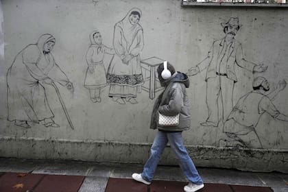 Una mujer pasa junto a un graffiti que representa a antiguos residentes de Teherán en el norte de Teherán, Irán, el lunes 27 de enero de 2025.