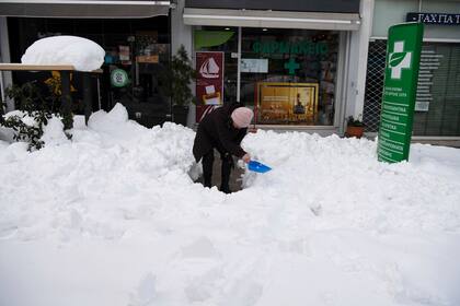 Una mujer quita la nieve afuera de una farmacia en Cholargos, suburbio de Atenas, después de una tormenta de nieve, el martes 25 de enero de 2022