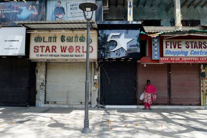 Una mujer se para frente a las tiendas cerradas en una calle comercial después del cierre preventivo contra la propagación del coronavirus, en Chennai, el 19 de junio de 2020