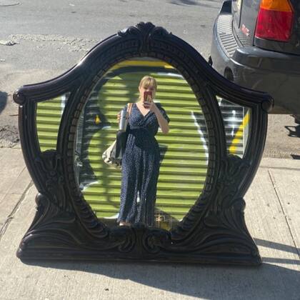 Una mujer se saca una foto frente a un trabajado espejo oval, en alguna vereda de la Gran Manzana