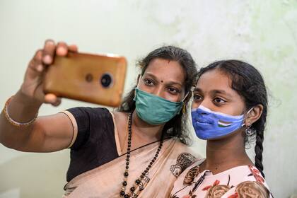 Una mujer se toma una selfie con su hija a quien un artista le pintó la cara con una mascarilla para crear conciencia sobre las medidas utilizadas para prevenir la propagación del coronavirus en Hyderabad, la India, el 20 de septiembre de 2020