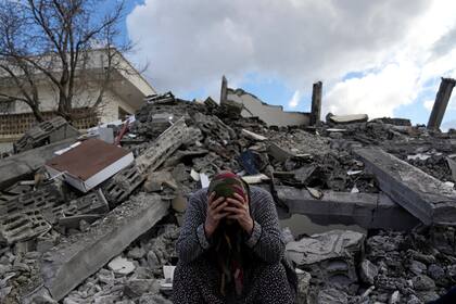 Una mujer sentada sobre los escombros mientras los equipos de rescate de emergencia buscan personas bajo los restos de los edificios destruidos en la localidad de Nurdagi, a las afueras de la ciudad de Osmaniye, en el sur de Turquía, el martes 7 de febrero de 2023.