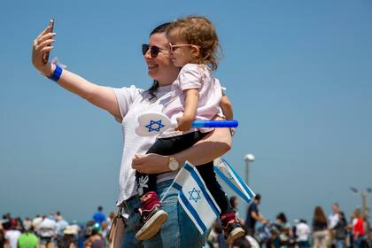 Una mujer sonríe mientras carga a un niño en Israel durante el Día de la Independencia el 15 de abril 2021. El país suspendió el uso de tapabocas obligatorio. 