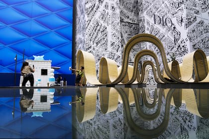 Una mujer sosteniendo una taza de café posa para una foto de recuerdo con una instalación de arte reflejada en un centro comercial de lujo al aire libre en Beijing, el miércoles 5 de junio de 2024.