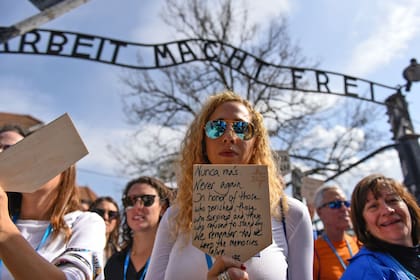 Una mujer sostiene un cartel con la frase "nunca más" en varios idiomas delante del ingreso al campo de concentración nazi Auschwitz
