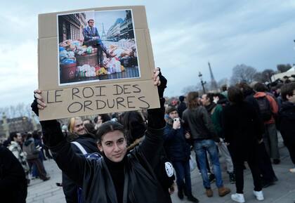 Una mujer sostiene un cartel con una imagen del presidente de Francia, Emmanuel Macron, sentado sobre una pila de basura con la frase "rey de la basura", durante una protesta en París, el 17 de marzo de 2023. 