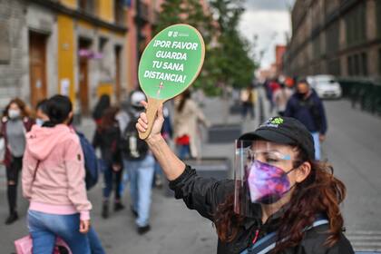 Una mujer sostiene un letrero que dice "Por favor, guarda tu sana distancia" en la Ciudad de México, el 18 de septiembre de 2020, en medio de la pandemia del coronavirus