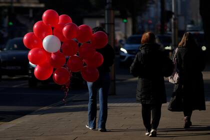 Una mujer sostiene una colección de globos rojos y uno blanco mientras camina hacia su automóvil, en Londres