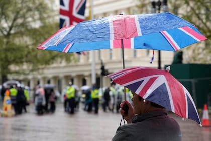 Una mujer tiene dos paraguas con la bandera británica mientras espera bajo la lluvia en el Mall, parte de la ruta de la Coronación en Londres