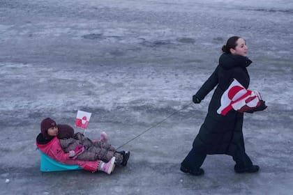 Una mujer tira de sus hijos en un trineo durante una protesta contra la política del presidente estadounidense Donald Trump hacia Groenlandia frente al consulado estadounidense en Nuuk, Groenlandia, el sábado 17 de enero de 2026. (AP Photo/Evgeniy Maloletka)