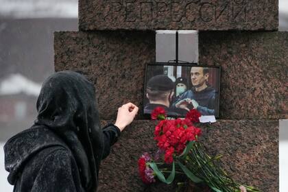 Una mujer toca la fotografía de Alexei Navalny tras dejar flores en homenaje al fallecido líder opositor ruso, en San Petersburgo, Rusia, el sábado 17 de febrero de 2024