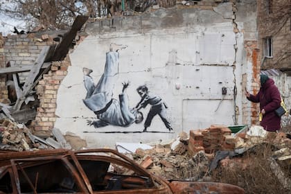 Una mujer toma una fotografía de una obra sobre la pared de un edificio destruido por los combates en Borodyanka, región de Kiev, Ucrania
