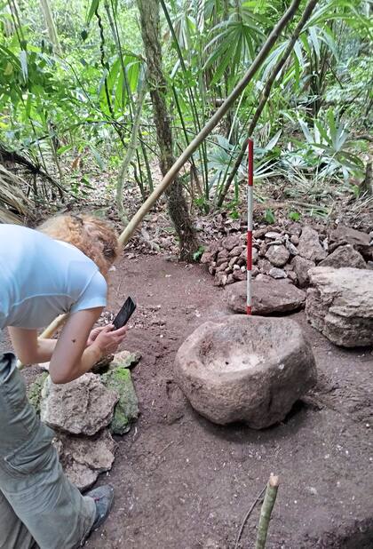 Una mujer tomando fotografías a una pieza descubierta en el yacimiento arqueológico de Uaxactún