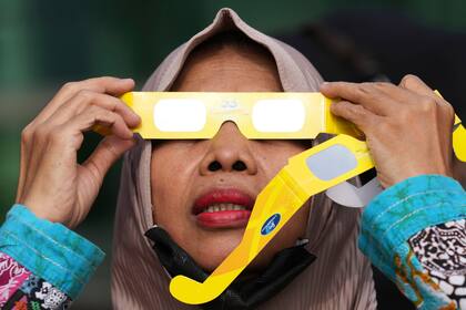 Una mujer utiliza gafas protectoras para ver un eclipse solar en Yakarta, Indonesia, el jueves 20 de abril de 2023. Los pocos afortunados en su ruta o bien vieron la oscuridad de un eclipse total o el “anillo de fuego” cuando el sol asomaba tras la Luna. (AP Foto/Tatan Syuflana)