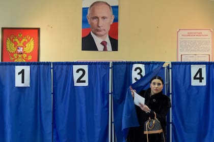 Una mujer vota en Donetsk, en la región ucraniana ocupada por Rusia, bajo la mirada de un poster de Putin 