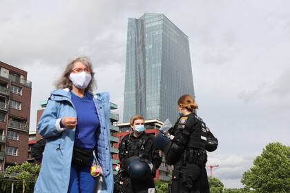 Una mujer y agentes de policía con máscaras faciales se muestran frente a la sede del Banco Central Europeo (BCE) durante una manifestación contra las restricciones vigentes para limitar la propagación del coronavirus el 23 de mayo de 2020 en Frankfurt