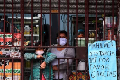 Una mujer y su hija, ambas con mascarillas como medida preventiva contra el nuevo coronavirus, miran la calle desde una tienda en la Villa 31, Buenos Aires, el 5 de mayo de 2020