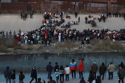 Una multitud de migrantes se reúne a orillas del río Bravo (Grande) el martes 20 de diciembre de 2022, frente al muro fronterizo en el El Paso, Texas, visto desde Ciudad Juárez, México. (AP Foto/Christian Chavez)
