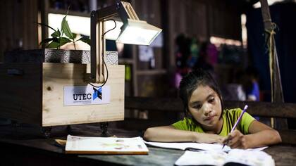 Una nena de la localidad de Nueva Saposoa, una comunidad indígena en Perú, hace la tarea usando la luz de una lámpara con energía provista por una planta