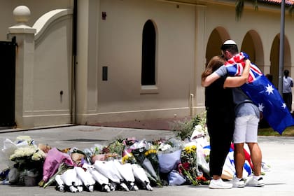 Una pareja coloca flores como homenaje a las víctima de un tiroteo ante el Bondi Pavilion en el distrito de Bondi Beach, Sydney, el lunes 15 de diciembre de 2025, al día siguiente de la balacera. (AP Foto/Mark Baker)