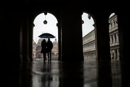 Una pareja se refugia contra la lluvia con un paraguas mientras caminan en la Plaza de San Marcos durante un día lluvioso en Venecia, el domingo 1 de marzo de 2020.