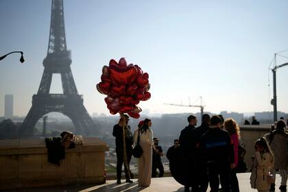 Una pareja sostiene globos rojos en forma de corazón frente a la Torre Eiffel, en París