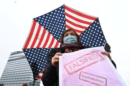 Una partidaria de la oposición georgiana sostiene un cartel y un paraguas con los colores de la bandera de los Estados Unidos mientras asiste a un mitin en el centro de Tbilisi el 18 de noviembre de 2020