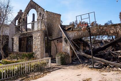 Una pelota de baloncesto se ve enganchada en la red delante de una casa destruida en el incendio de Palisades en el vecindario de Pacific Palisades en Los Ángeles, el viernes 24 de enero de 2025. (AP Foto/Damian Dovarganes)