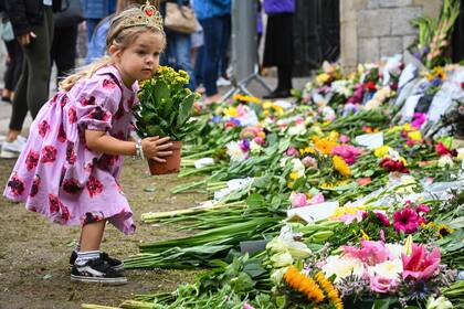 Una pequeña niña coloca una maceta con flores cerca de una zona de tributo a las afueras del Castillo de Windsor
