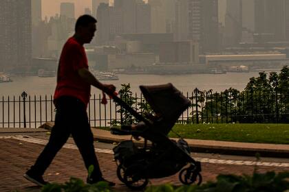 Una persona camina con un cochecito en un parque frente al horizonte de la ciudad de Nueva York, ya que está cubierto de neblina y humo de los incendios forestales de Canadá el 7 de junio de 2023 en Weehawken, Nueva Jersey