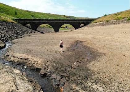 Una persona camina por una orilla seca de un afluente del embalse de Dowry, cerca de Oldham, Inglaterra, el lunes 18 de julio de 2022, mientras continúa la ola de calor en el Reino Unido. 