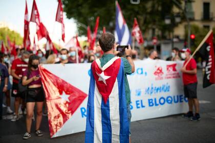 Una persona con la bandera de Cuba en la espalda saca una fotografía a una gran pancarta en una manifestación contra el embargo económico de Estados Unidos sobre Cuba, a 24 de julio de 2021, en Madrid