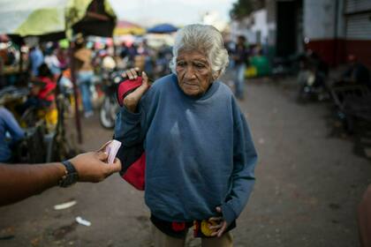 Una persona le ofrece dinero en efectivo a una mujer mientras suplica en Caracas