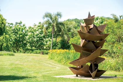 Una pila de sueños, una obra en hierro que pertenece a la serie De la rivera, de Alberto Bastón Díaz, rodeada por hemerocallis, palmeras y catalpas. 
