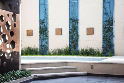 Una placa de metal oxidada diseñada especialmente se sumó a la ambientación del jardín. En el muro, chapones cuadrados con luz por detrás.
