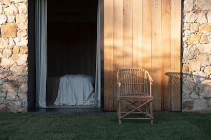 Una puerta corrediza de madera y una silla de ratán enmarcan la calma del dormitorio que se abre directamente al jardín.