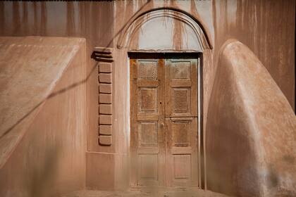 Una puerta tallada en una casa blanqueada de La Poma, chorreada de rojo, el color del adobe. Típica arquitectura vallista.