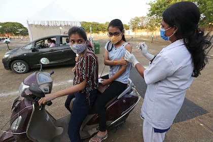 Una trabajadora de la salud inocula a dos jóvenes en Nueva Delhi