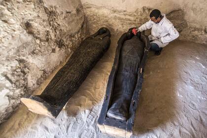 Un arqueólogo egipcio cepilla una momia puesta dentro de un sarcófago de madera negro tallado con incrustaciones doradas