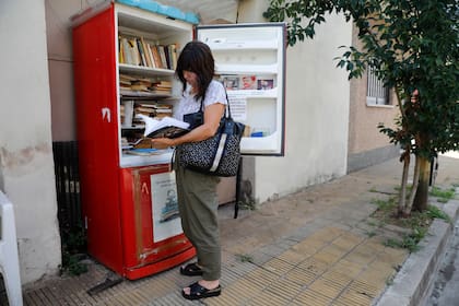 Una vecina del pasaje Praga, en Parque Chas, revisa los libros de la Biblioteca Libre de Praga, instalada en una vieja heladera