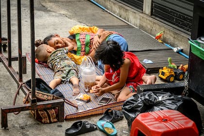 Una vendedora de comida callejera descansa mientras sus hijos juegan detrás de su carrito después de que se levantaran las restricciones para detener la propagación del coronavirus en Bangkok, Tailandia, el 18 de mayo de 2020