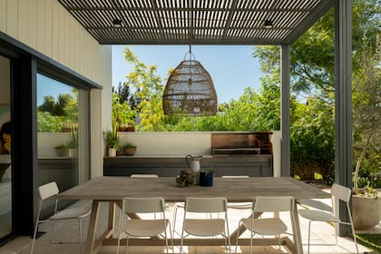 Una viga de hierro atraviesa el living, donde sostiene la chimenea, y avanza hacia la galería como soporte de la estructura de la parrilla. El detalle refuerza la continuidad entre interior y exterior que proponen las aberturas.